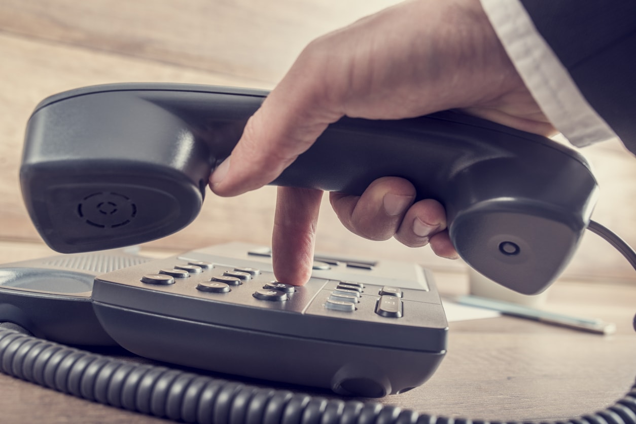 La téléphonie : un téléphone IP Cisco poser sur une table et un homme qui compose un numéro avec le cornet en main.