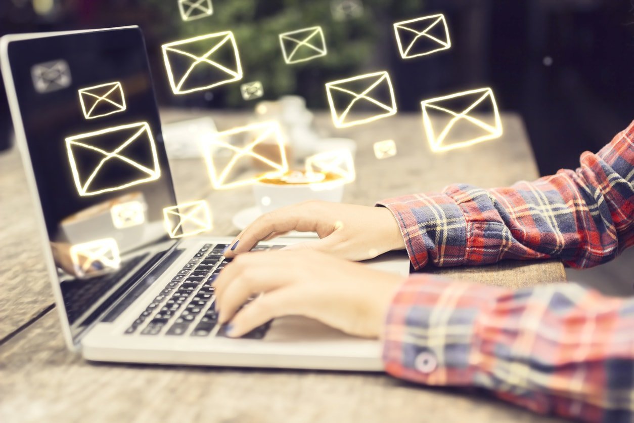 Contact : un utilisateur écrit un Email sur son ordinateur portable et des icônes d'enveloppes illuminées sortent de l'écran.