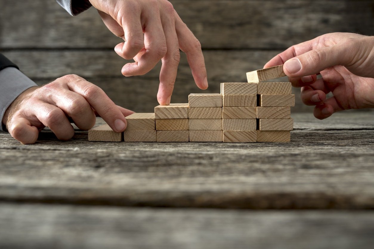 Croissance : des réglettes en bois sont disposées en forme d'escalier et les deux doigts d'une main monte les échelons.